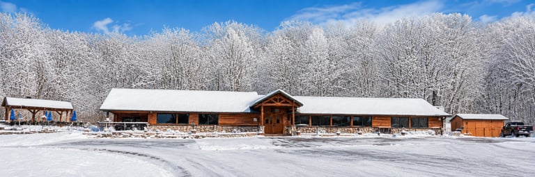 Snow-covered wooden ranch buildings with frost-covered trees and clear blue sky in winter landscape