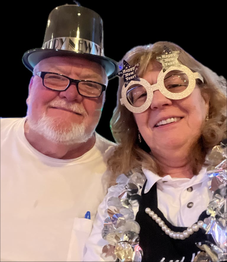 Two people wearing novelty party glasses and hats smile for a photo against a black background