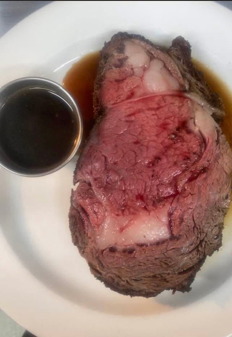 Sliced prime rib steak with medium-rare interior on white plate with au jus sauce in small bowl