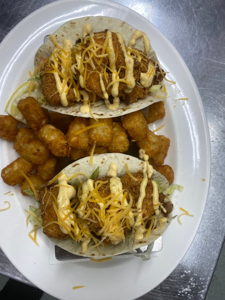 Two crispy fish tacos with shredded cabbage and fried potato balls on a white plate