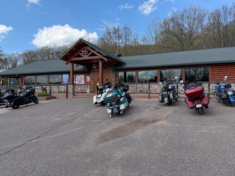 Motorcycles parked outside a rustic wooden building with a covered porch entrance on a clear day