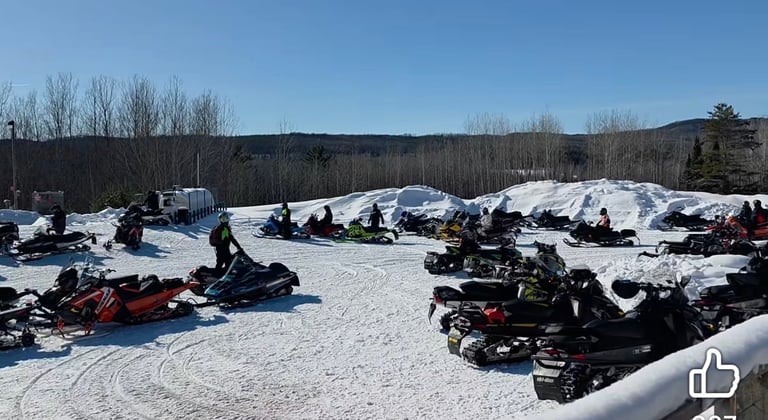 Snowmobile parking lot with dozens of snowmobiles lined up in snowy field, mountains and bare trees in background