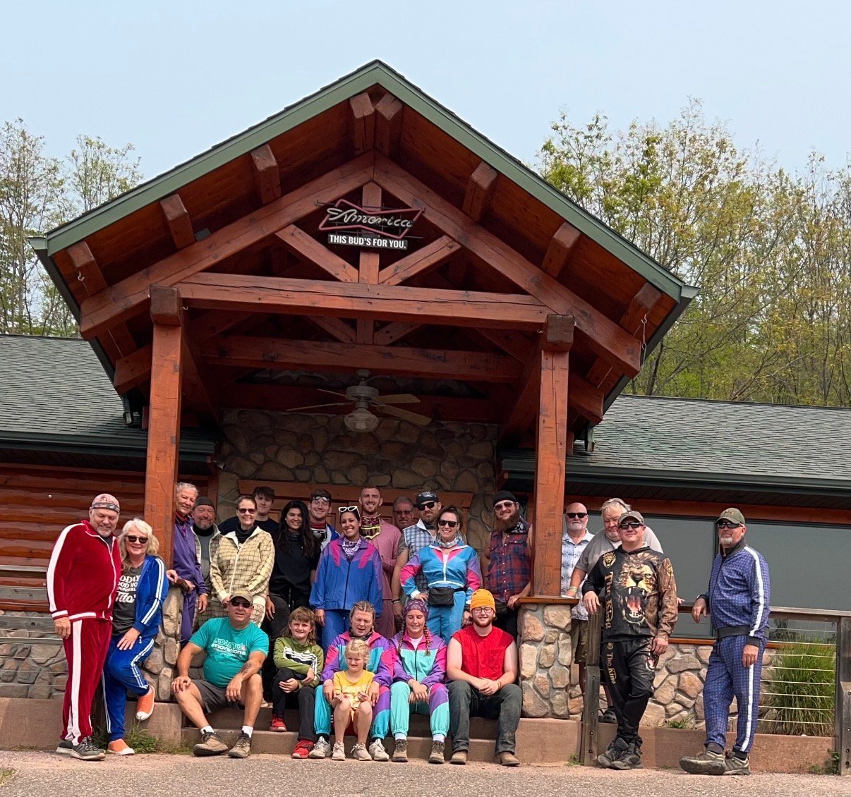 Large group of people posing together in front of a red wooden lodge building with stone accents