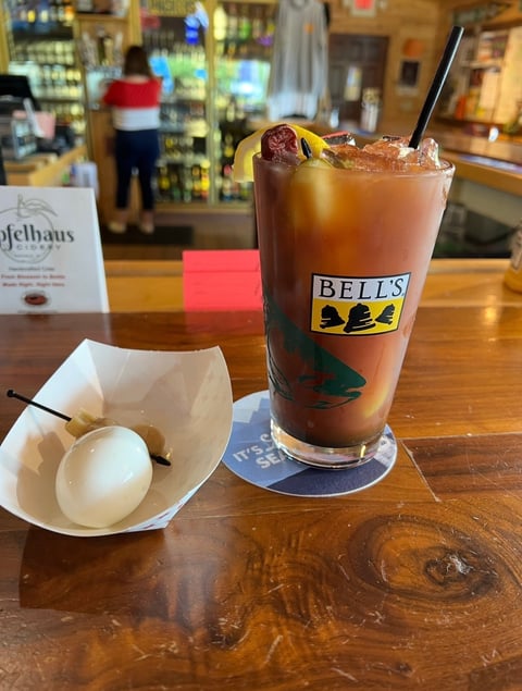 A Bells whiskey cola cocktail in a tall glass with ice and a cherry garnish, served at a wooden bar counter