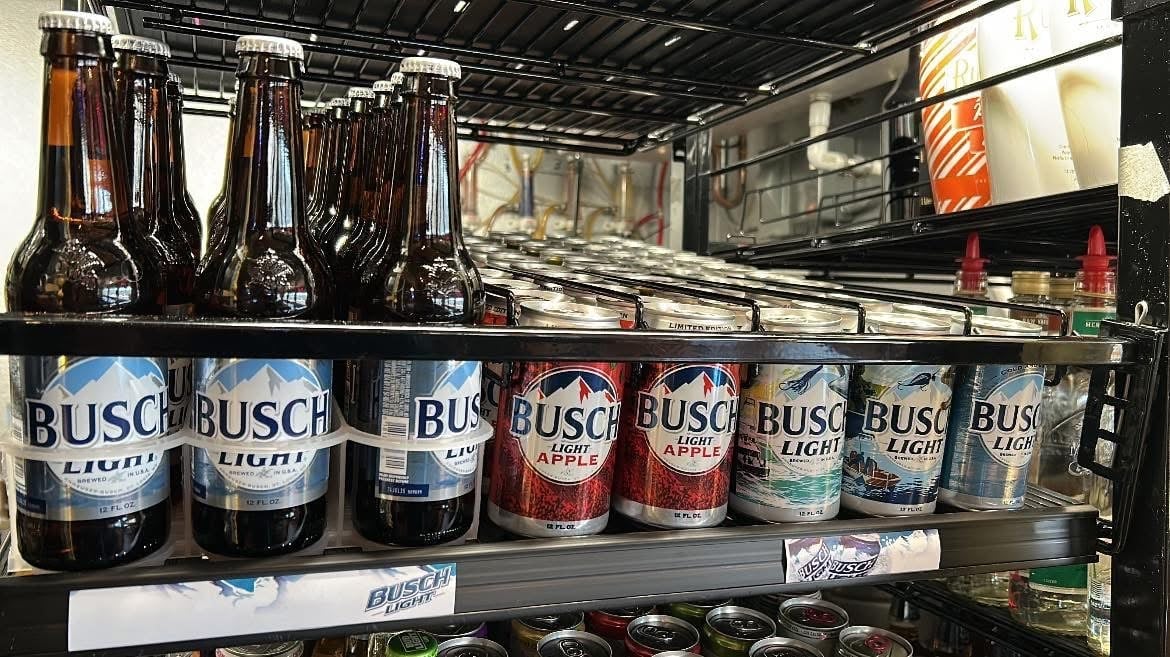 Assorted Busch beer bottles displayed on metal shelving in a retail cooler