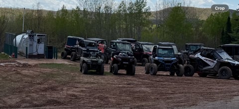 Row of off-road vehicles and equipment parked in dirt lot with trees in background