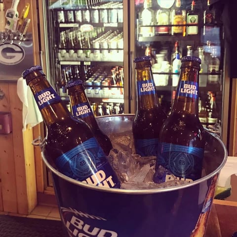 Bud Light beer bottles in ice bucket display in front of bar with illuminated shelves