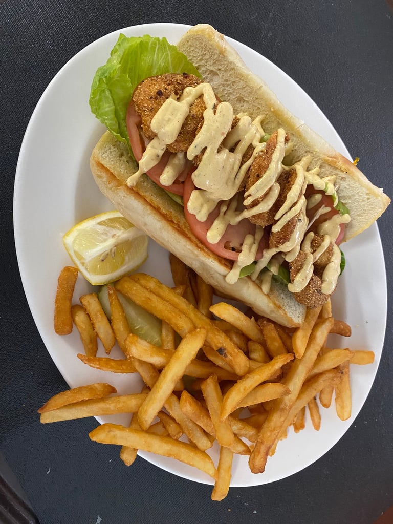 Breaded chicken sandwich with lettuce, tomato, and sauce on white plate with french fries and lemon wedge