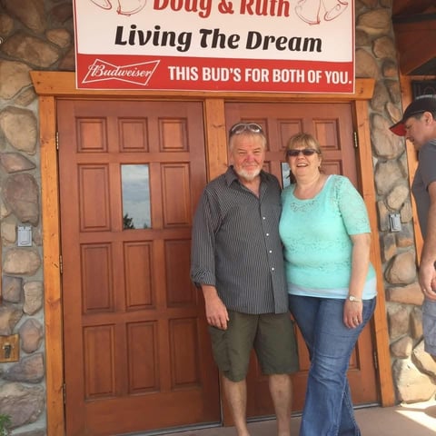 Two people standing in front of wooden doors beneath a Budweiser Body and Ruin Living the Dream bar sign