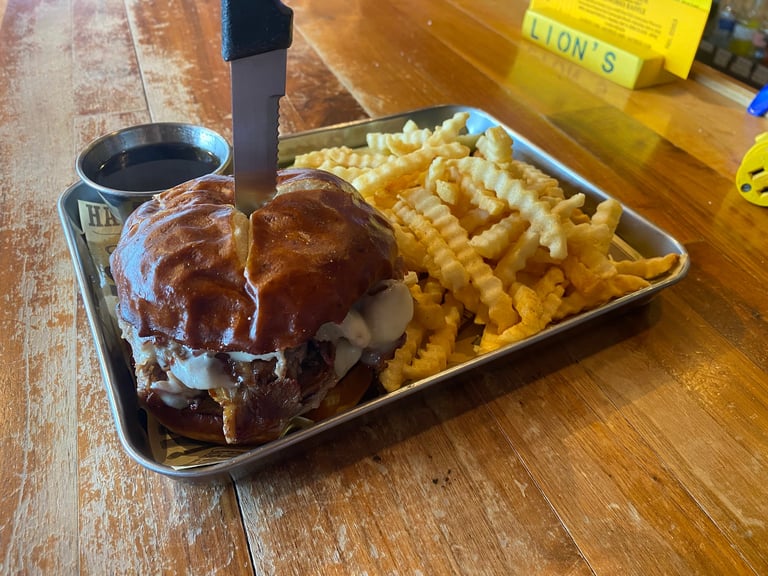Burger with caramelized glaze and crispy waffle fries served on a wooden table with a small cup of sauce
