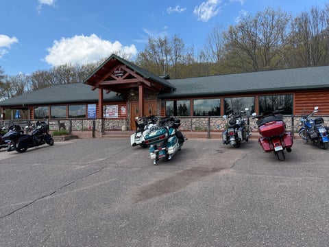 Motorcycles parked in front of a wooden lodge-style building with a covered porch and bare trees in background