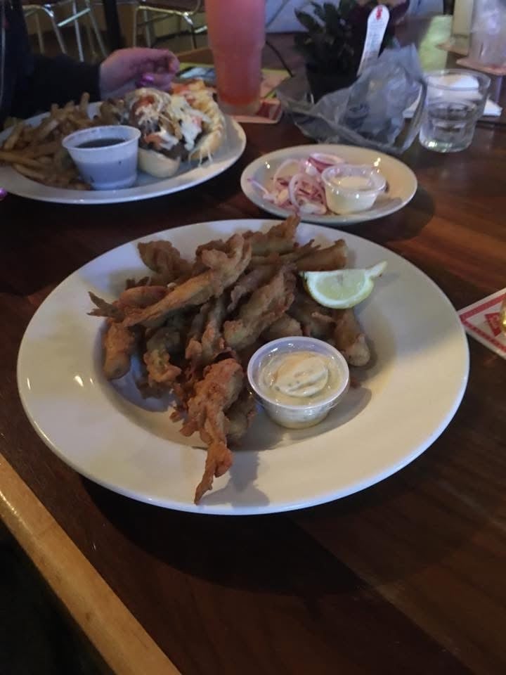 Plate of fried calamari with white sauce and lime wedge, surrounded by other seafood dishes on a wooden table